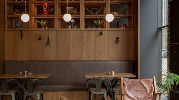 A cozy cafe with wooden tables and chairs, pendant lighting, and shelves with plants and decor.