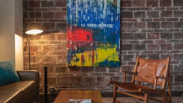 A room with a brick wall, a colorful abstract painting, a wooden coffee table, a red sofa, and a leather couch.