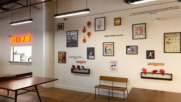 A room with a ping pong table, benches, and various framed pictures and posters on the walls.