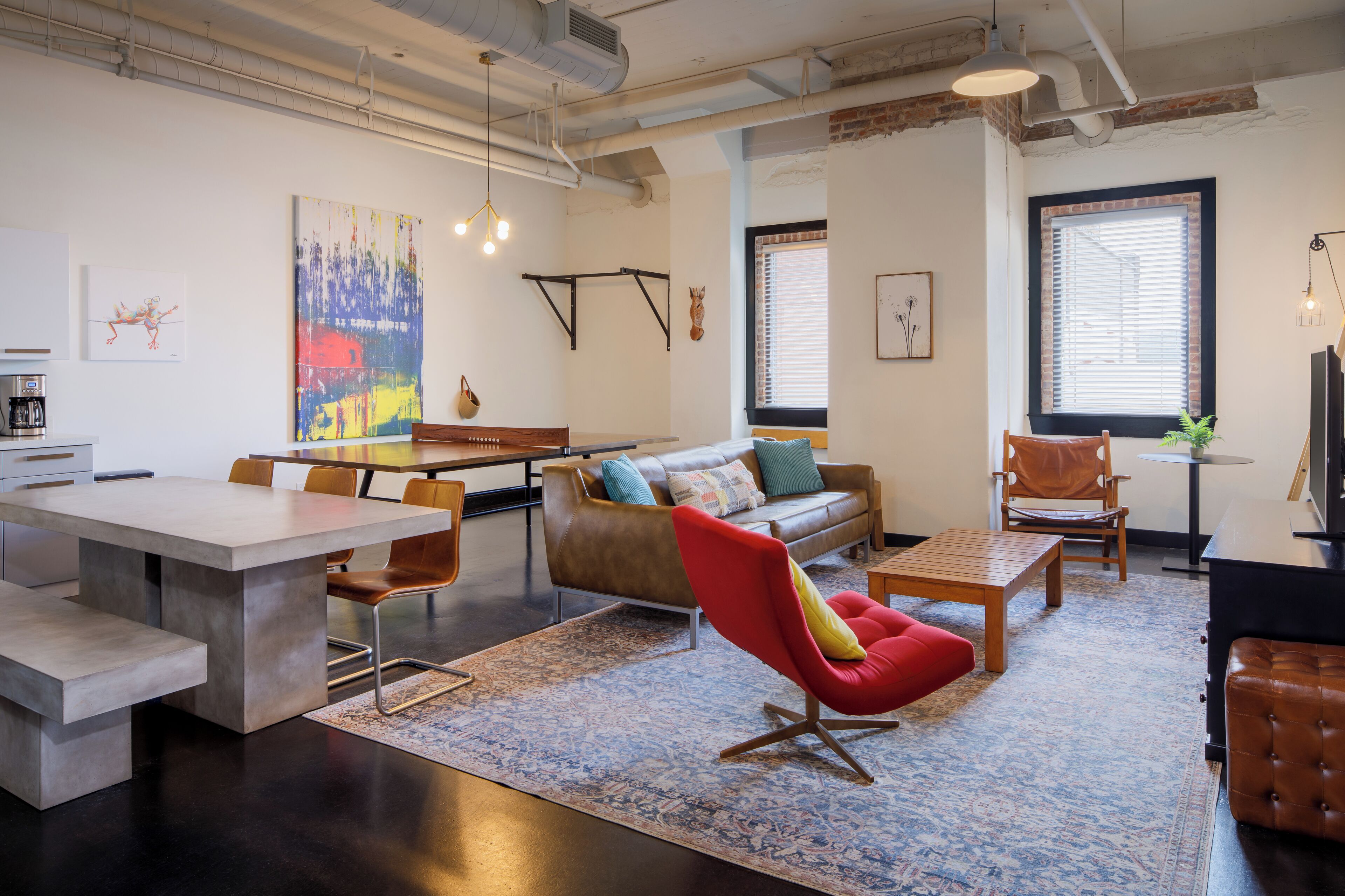 Un espace de vie moderne comprenant un coin repas, un canapé, un fauteuil rouge et une table basse.
