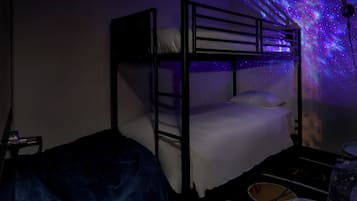 Un lit superposé avec un projecteur lumineux qui projette des étoiles sur le mur, une petite table avec une chaise et une couverture sur le sol.