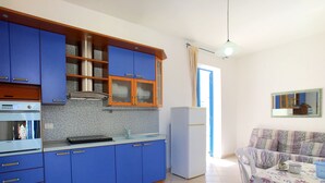 A compact kitchen with blue cabinets, a white refrigerator, and a dining area with a floral tablecloth.