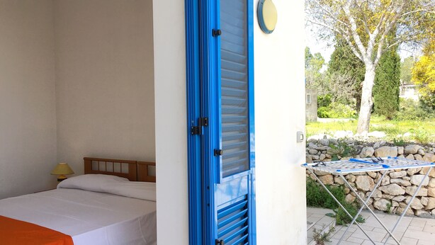 A bedroom with a bed, a blue door, and a view of a garden with a stone wall and a tree.