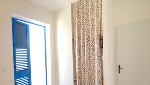 A bedroom with a bed, a blue door, a white door, and a curtain with a floral pattern.