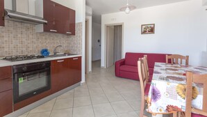 A kitchen with a stove, oven, and cabinets, a dining table with chairs, and a red sofa in a living area.