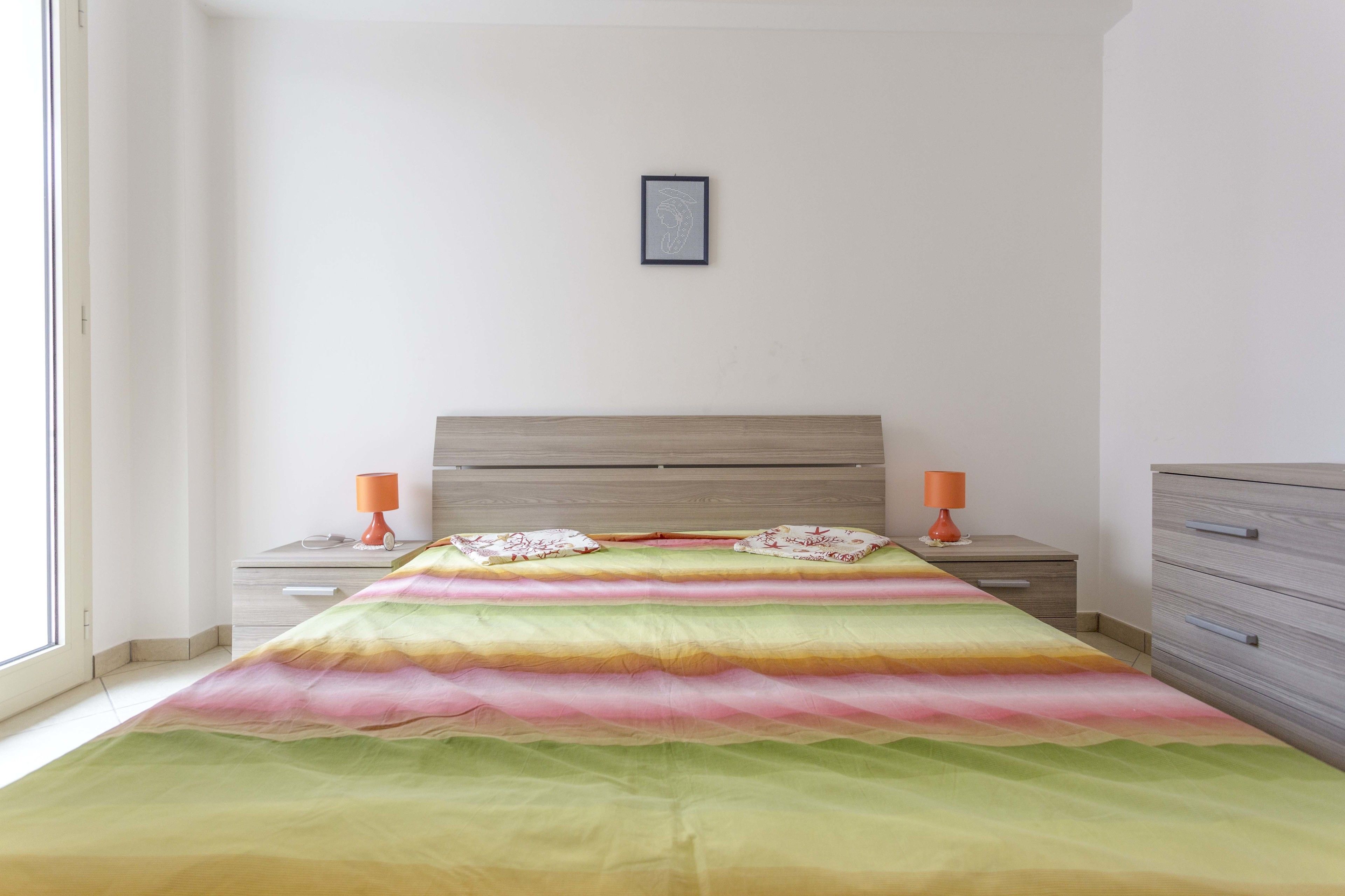Un dormitorio con una cama, dos mesitas de noche, un aparador y un cuadro en la pared.