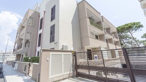 A modern apartment building with multiple balconies, a gated entrance, and a clear sky.