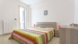 A bedroom with a bed, bedside tables, a dresser, a radiator, and a door to a balcony.