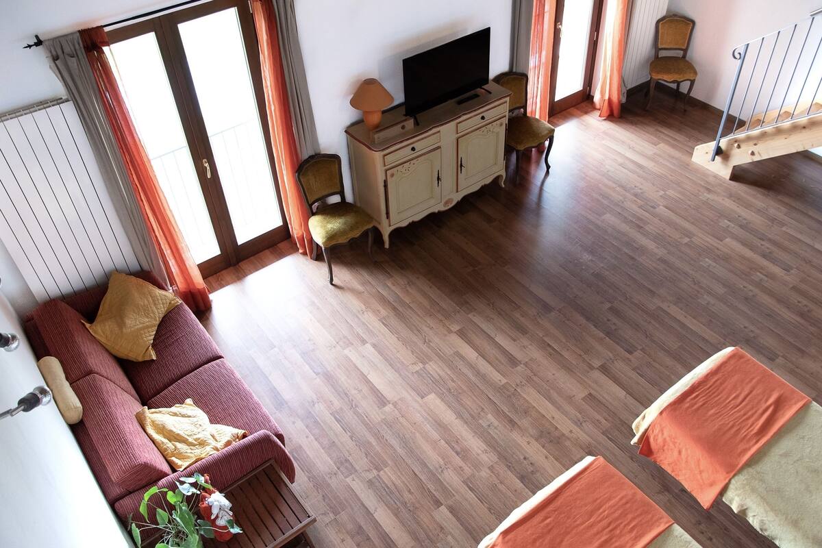 Ein geräumiges Wohnzimmer mit Holzboden, einer Couch, einem Fernseher auf einem Schrank und einer Treppe.