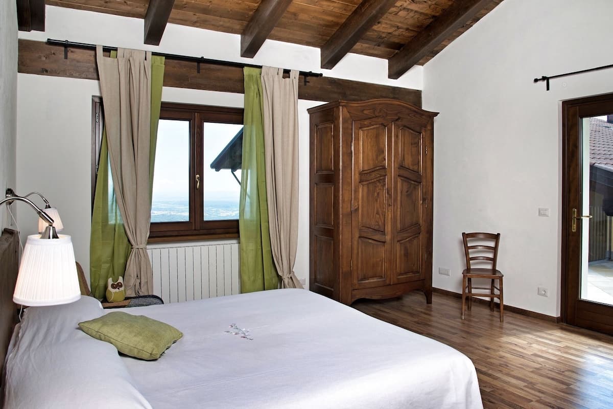 Ein Schlafzimmer mit einem Bett, einem Holzschrank, einem Sessel und einem Fenster mit Vorhängen.