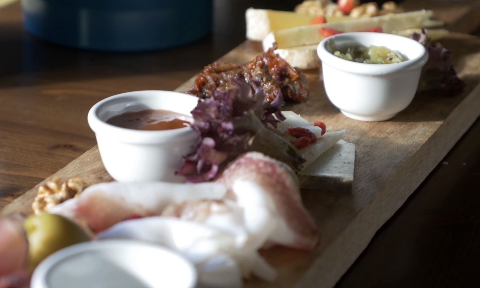 A wooden board with various food items and small bowls of sauces.