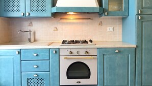 A kitchen with teal cabinets, a white stove, and a built-in oven. - Bilocale Rosalba (Gallipoli)