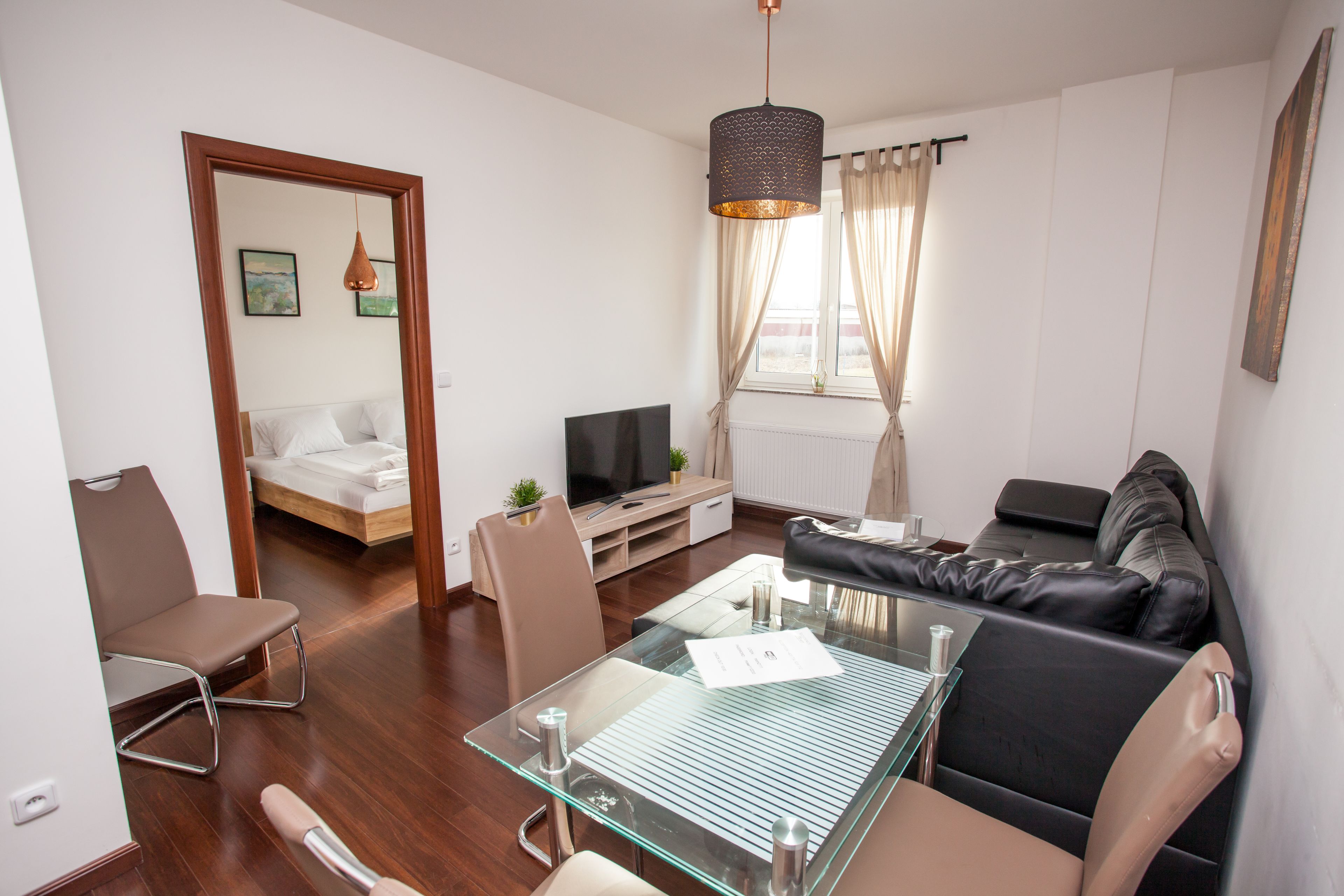 A modern hotel room with a glass dining table, leather sofa, and a TV.