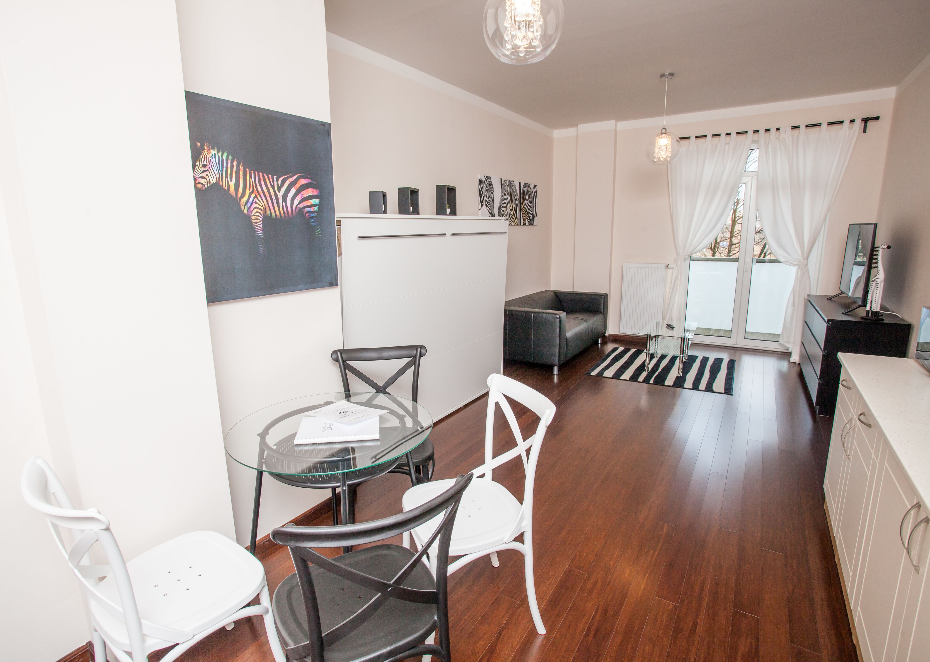 A modern living room with a glass dining table, a sofa, and a large window with curtains.
