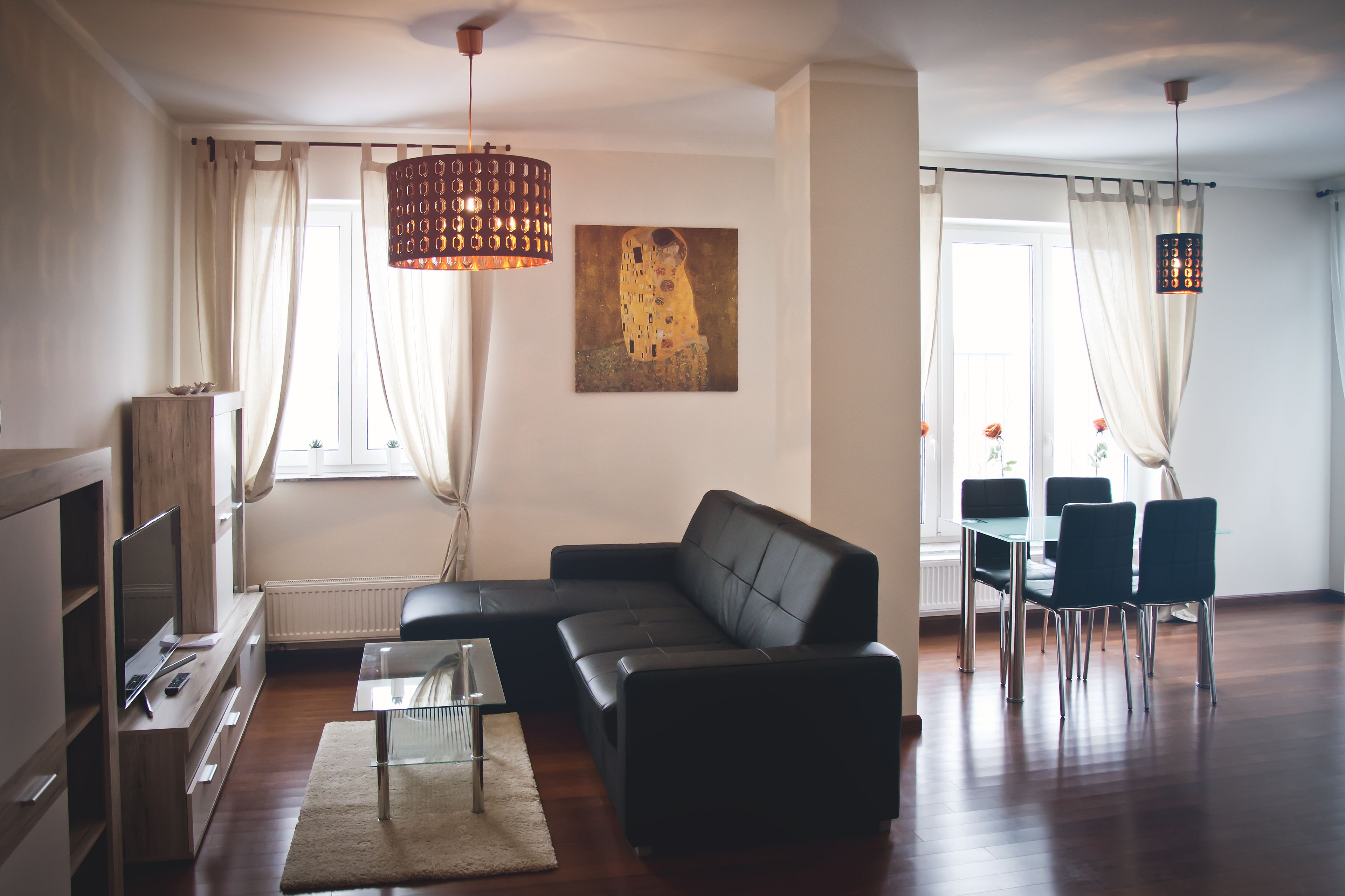 Una sala moderna con un sofá de cuero negro, una mesa de centro de vidrio y un comedor con mesa y sillas.