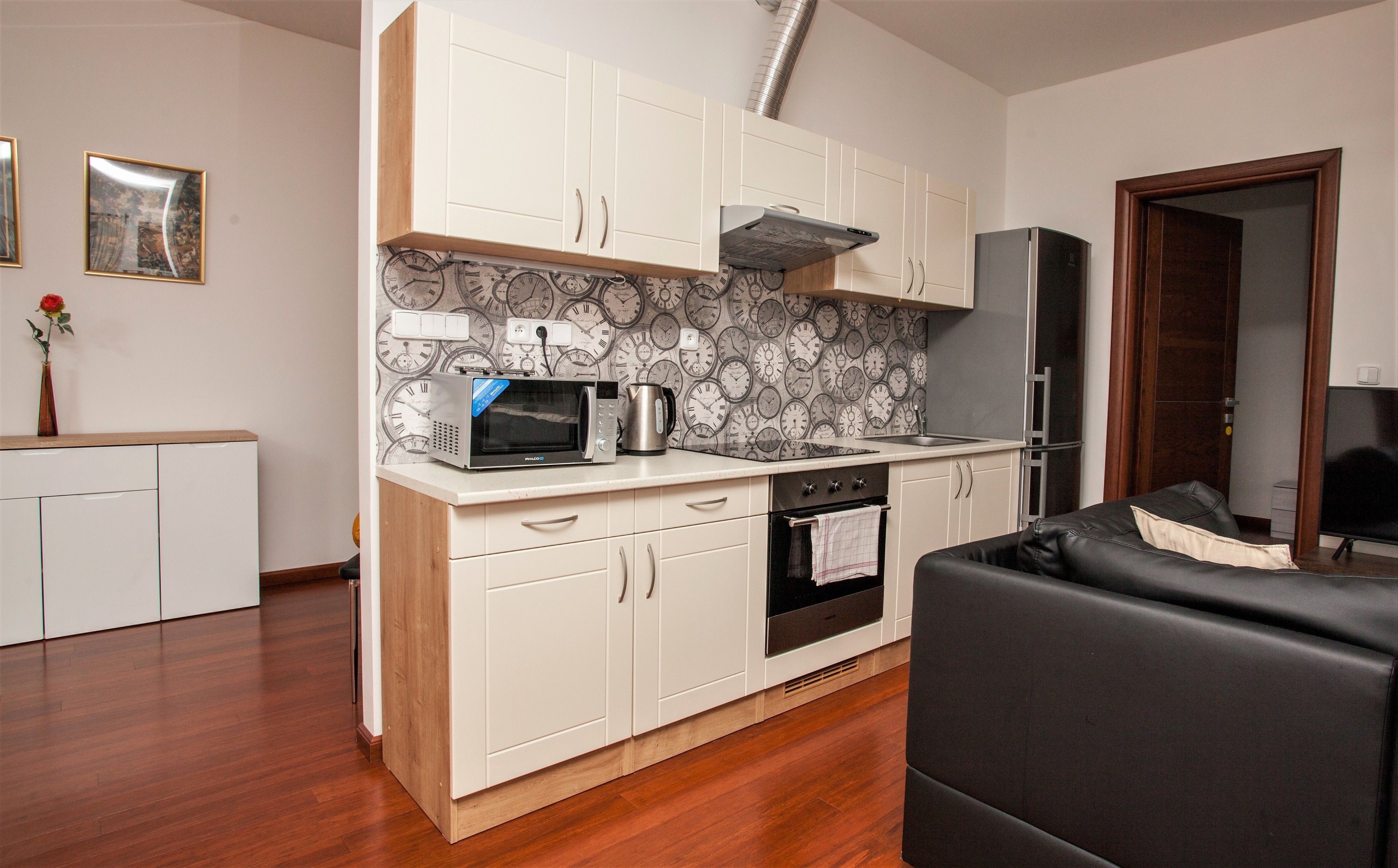 Una cocina compacta con armarios blancos, microondas, hervidor y refrigerador.