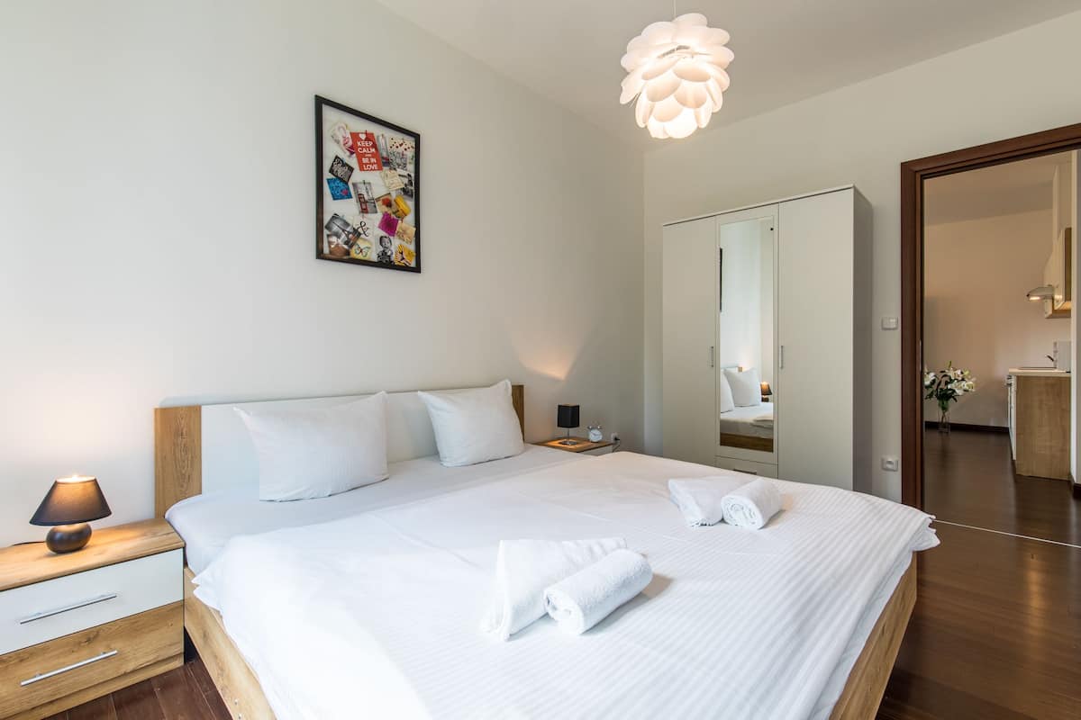Un lit bien fait, avec du linge de lit et des serviettes blanches, une lampe de chevet, un tableau encadré au mur et un grand miroir sur la porte.