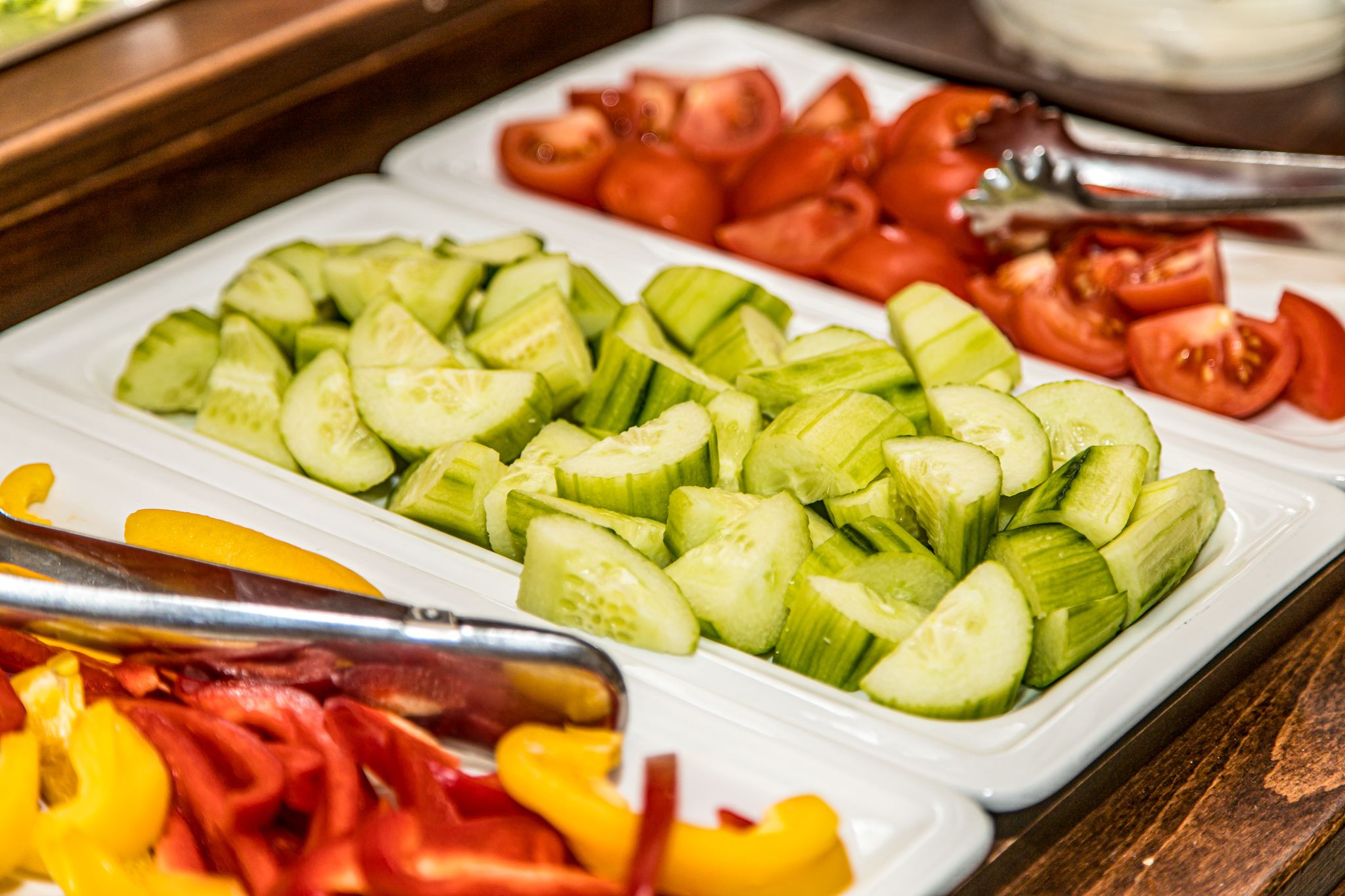 A buffet with sliced cucumbers, tomatoes, and bell peppers.