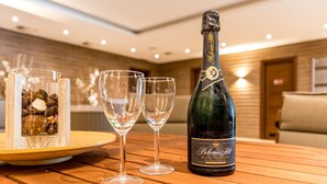 A bottle of Bohemia Selis Blang Dehors champagne on a wooden table with two empty glasses and a decorative glass container with pinecones.