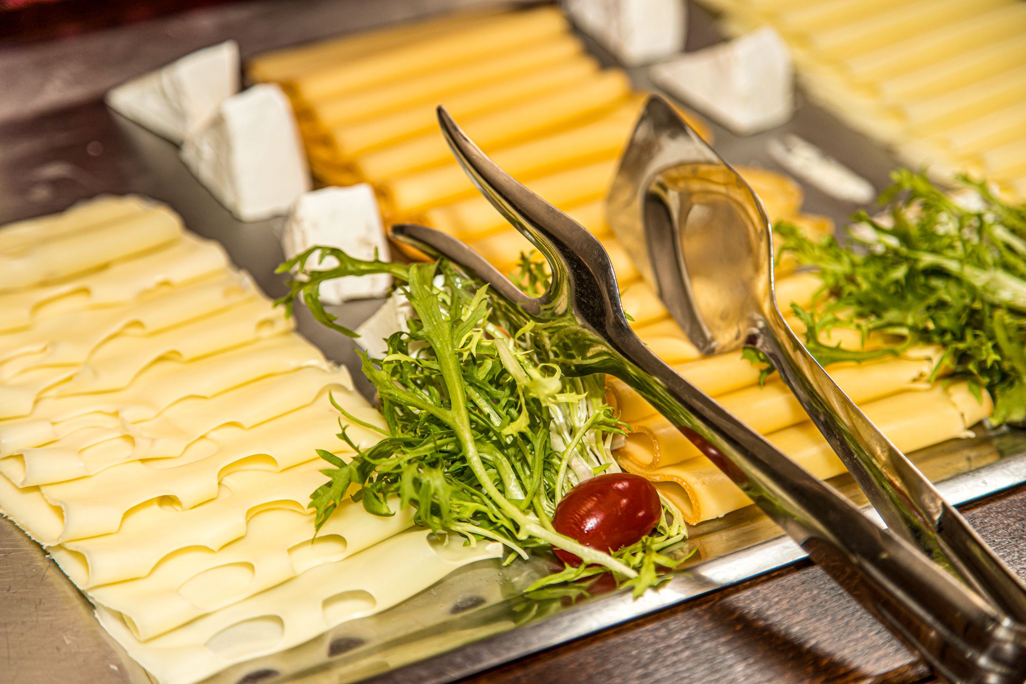 A cheese board with various cheeses, greens, and a cherry tomato.