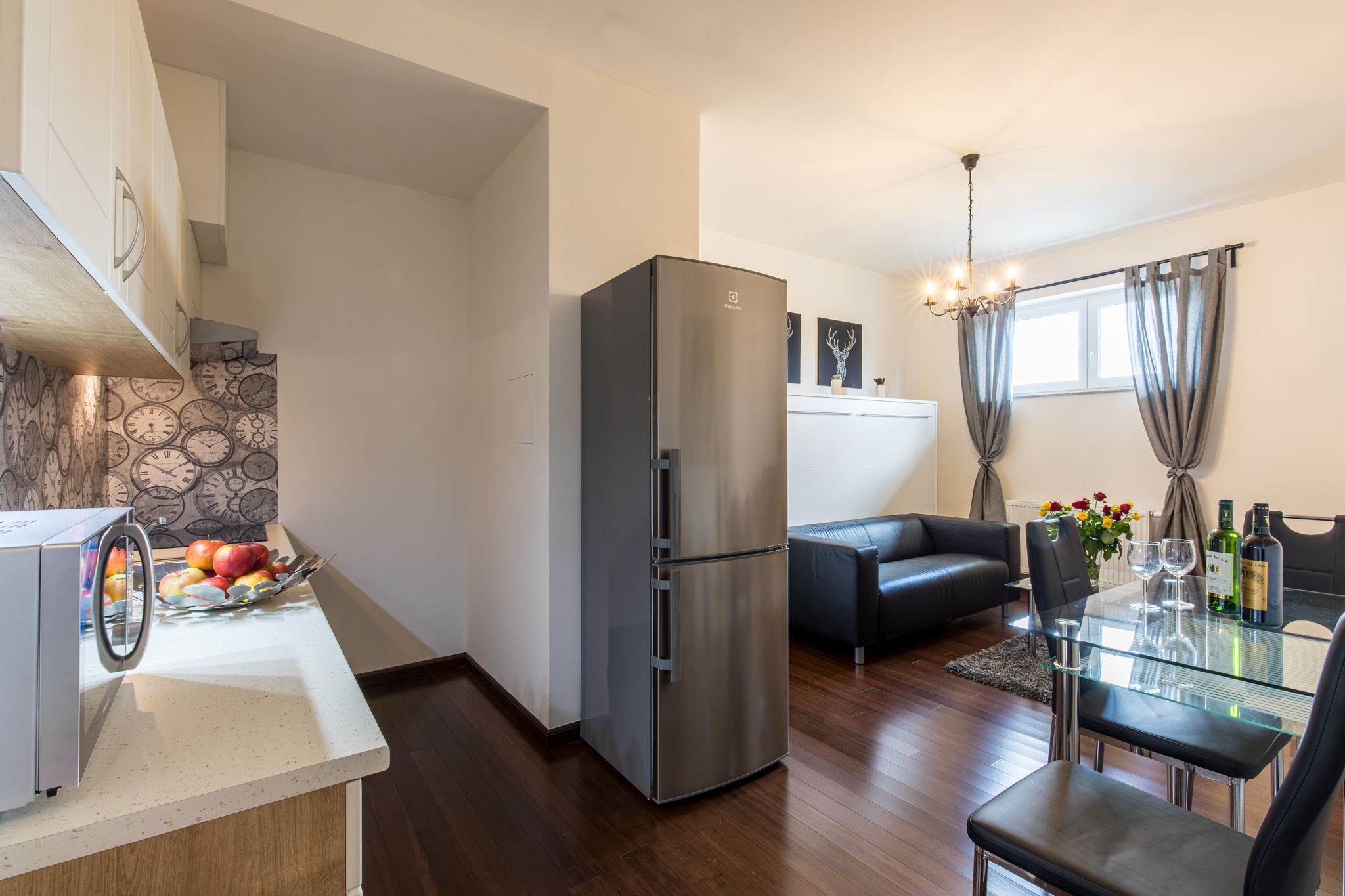 Eine moderne Küche mit einem Edelstahl-Kühlschrank, einem Essbereich mit Glastisch und einem schwarzen Ledersofa.