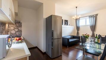 Eine moderne Küche mit einem Edelstahl-Kühlschrank, einem Essbereich mit Glastisch und einem schwarzen Ledersofa.