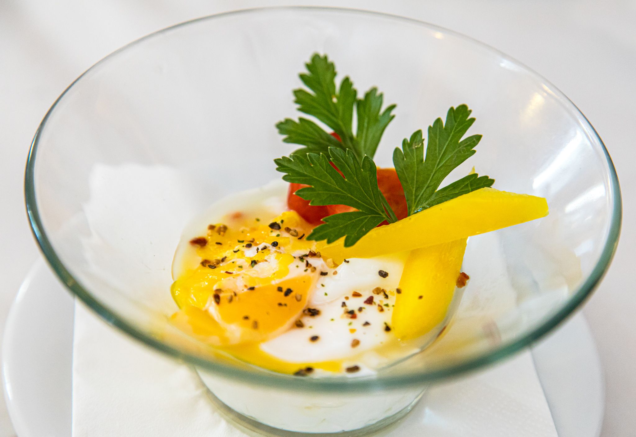 A clear glass bowl containing a dish with egg, tomato, and parsley.