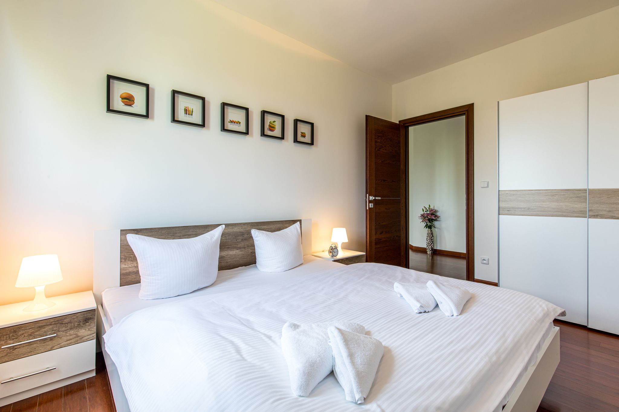 A neatly made bed with white linens and two pillows, a bedside table with a lamp, and a wooden headboard.