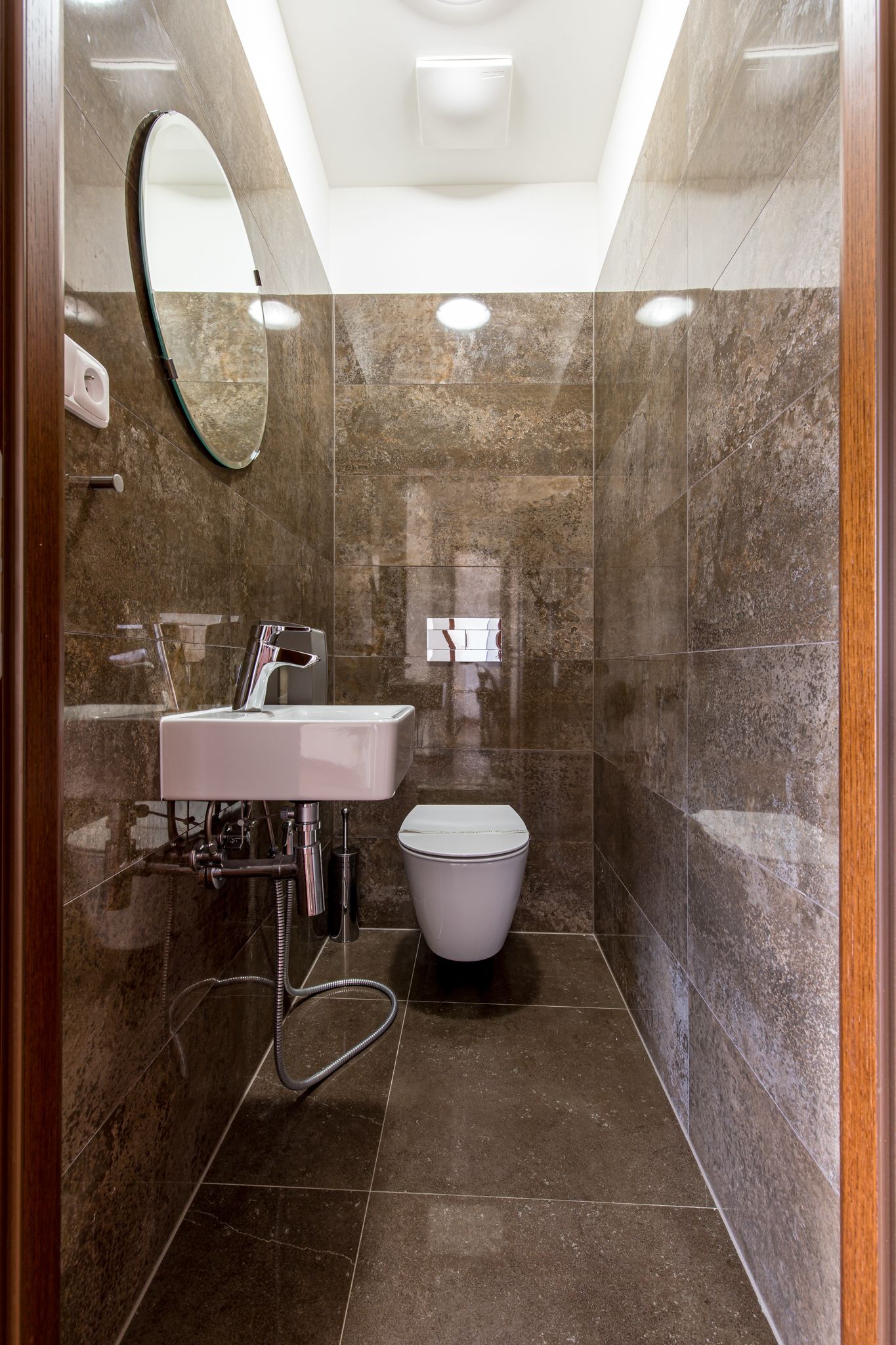 A modern bathroom with a marble floor, a white sink, a toilet, and a mirror.