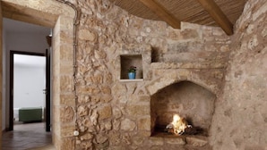 A stone fireplace with a fire, a small shelf with a plant, and a wooden ceiling beam. - Bilocale Rurale in Resort (Morciano di Leuca)