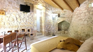 A stone-walled room with a bed, a TV mounted on the wall, and a fireplace. - Bilocale Rurale in Resort (Morciano di Leuca)