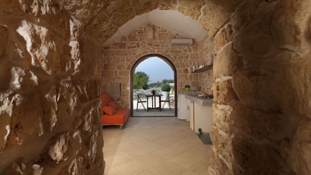 A stone-walled room with a view through an archway to an outdoor seating area. - Bilocale Rurale in Resort (Morciano di Leuca)