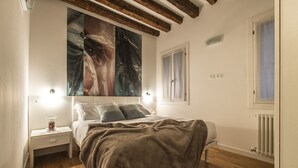 Ein Schlafzimmer mit einem Bett, Nachttischen, einem großen abstrakten Gemälde, einem Fenster und einer Heizung.