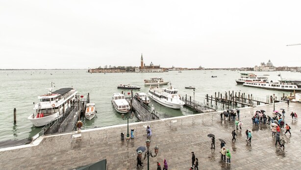 Eine Uferpromenade mit vertäuten Booten, einem Steg und Spaziergängern.