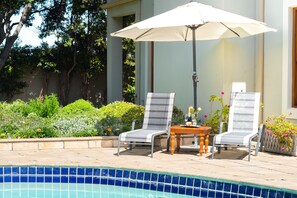 A poolside area with two lounge chairs, a table, and an umbrella.