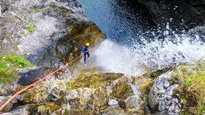 Una persona descendiendo en rápel por un risco rocoso hacia el agua.