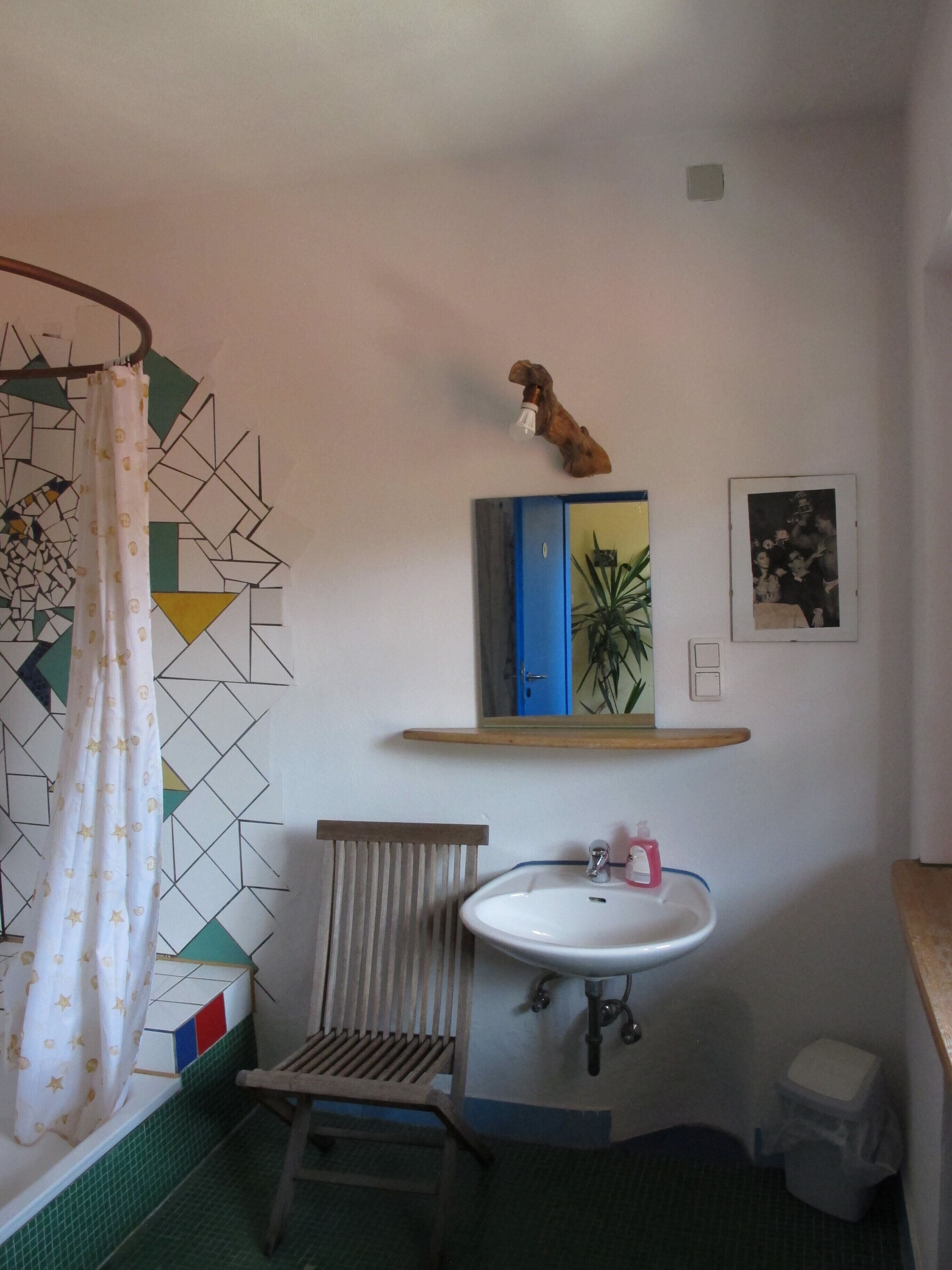 Un baño con cortina de ducha, un lavabo, una silla, un espejo y una estantería con una planta.