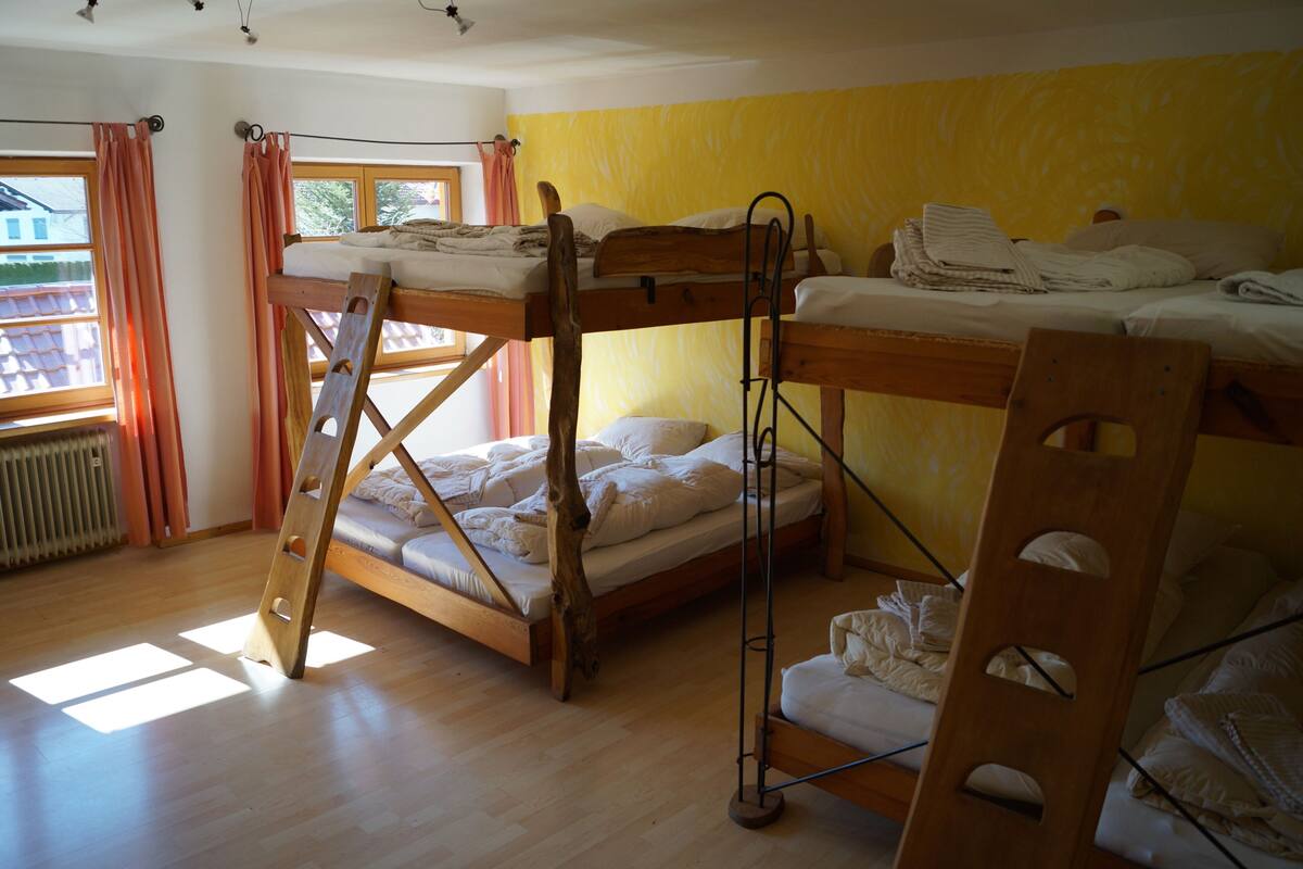 Una habitación con literas, una escalera de madera y una ventana con cortinas.