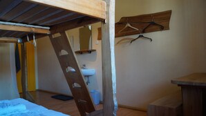 Una cama litera con escalera de madera, un escritorio de madera, un perchero y un lavamanos en una habitación con suelo de madera.