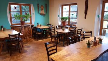 A cozy restaurant with wooden tables and chairs, potted plants, and large windows.