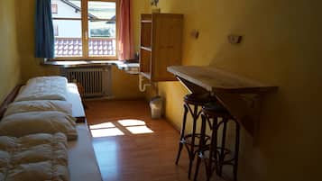 Una habitación pequeña con una cama, una mesa de madera y un ventanal con cortinas.