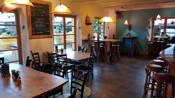 Ein Restaurantinnenraum mit Holztischen und -stühlen, hängenden Pendelleuchten und einer Kreidetafel mit Speisekarte.