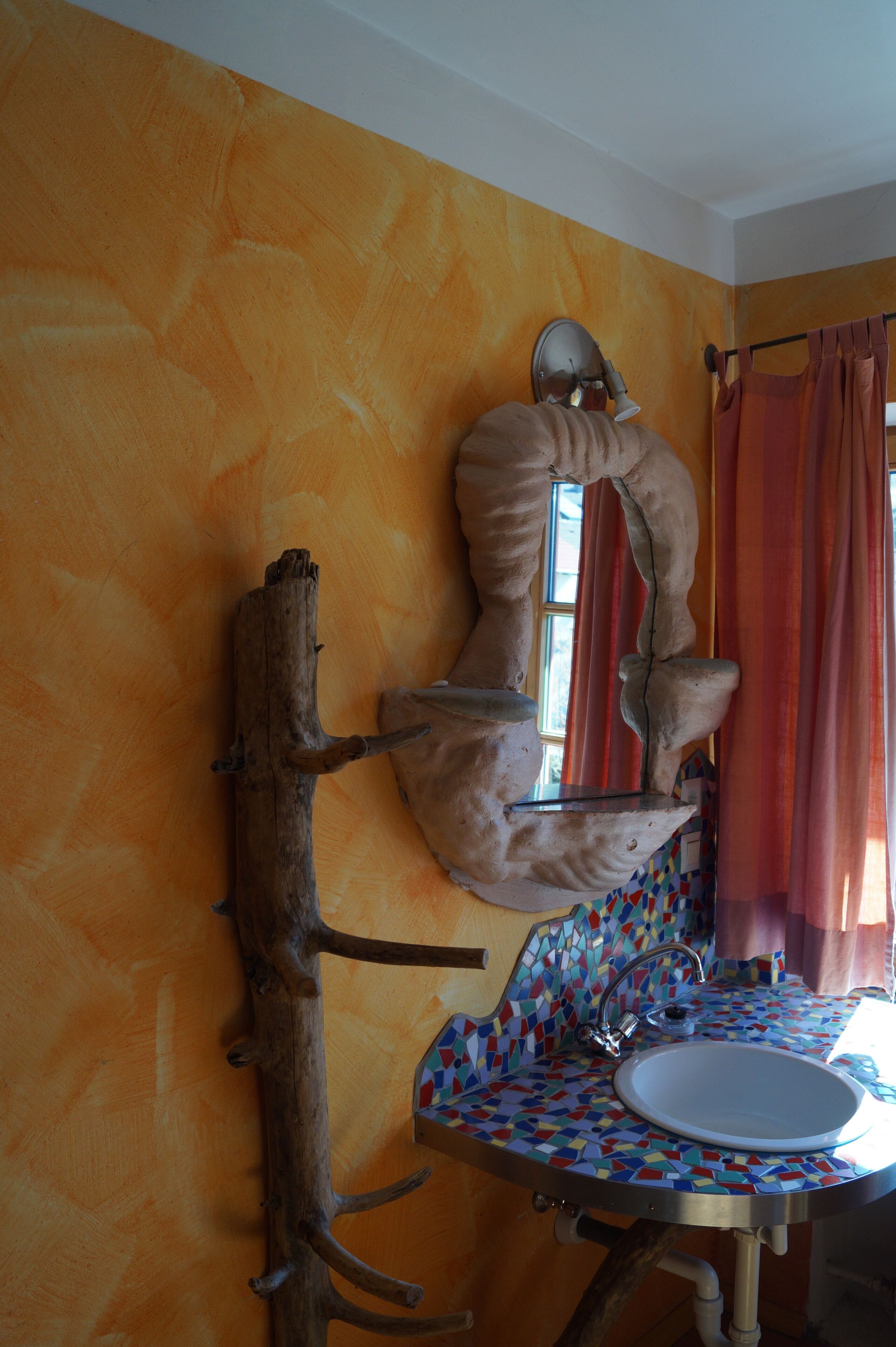 Casa de banho com uma escultura de madeira única, lavatório em mosaico e janela com cortinas.