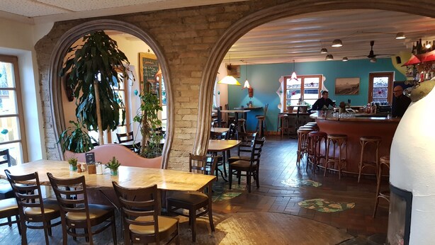 Un restaurante con mesas y sillas de madera, arcos de ladrillo y una zona de bar.