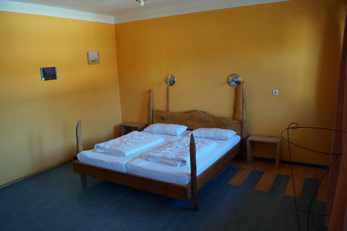 Una habitación con una cama de madera, dos mesitas de noche y una lámpara fijada a la pared.