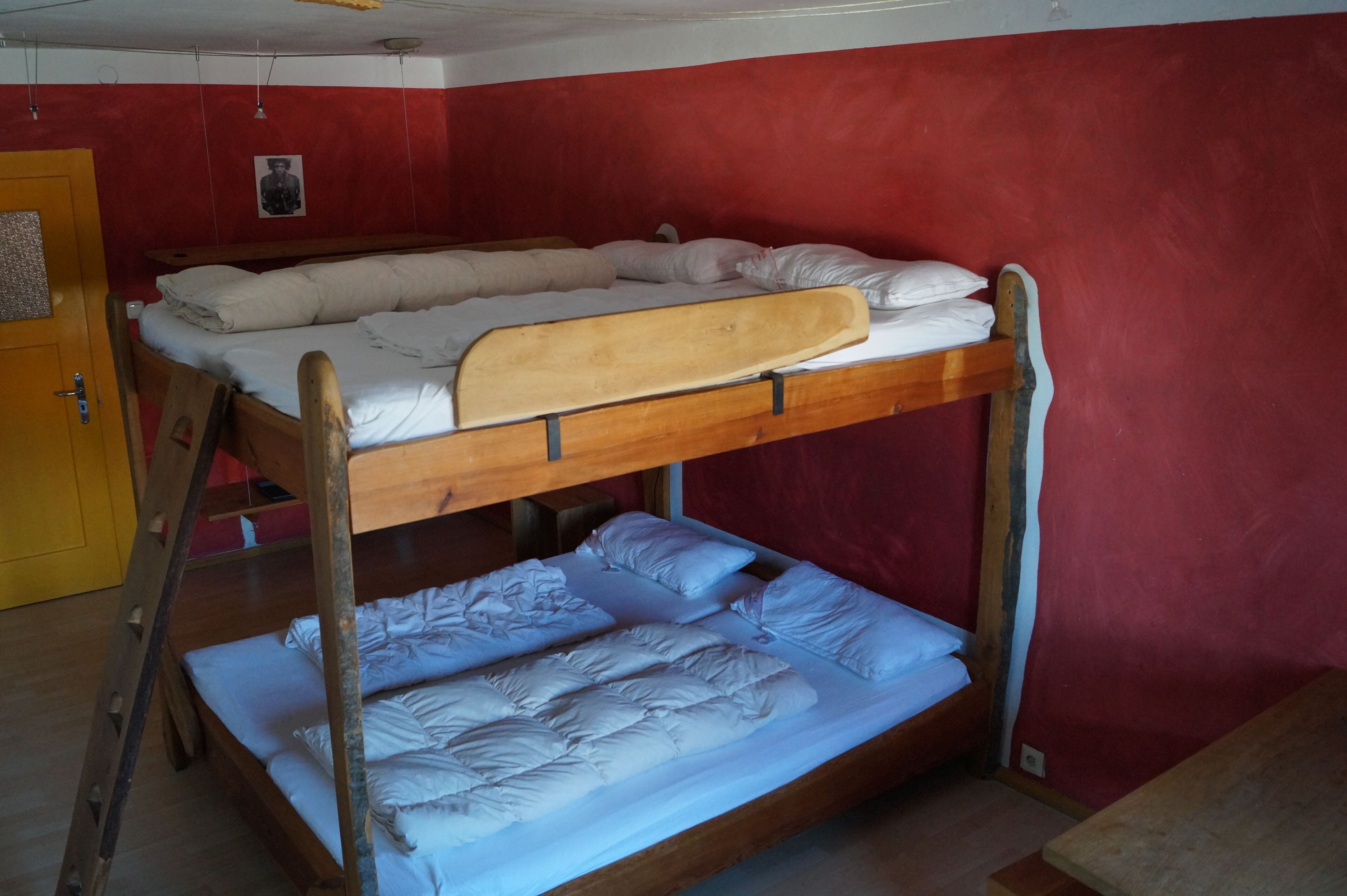 Una cama individual con dos literas, una escalera de madera y una pared roja.