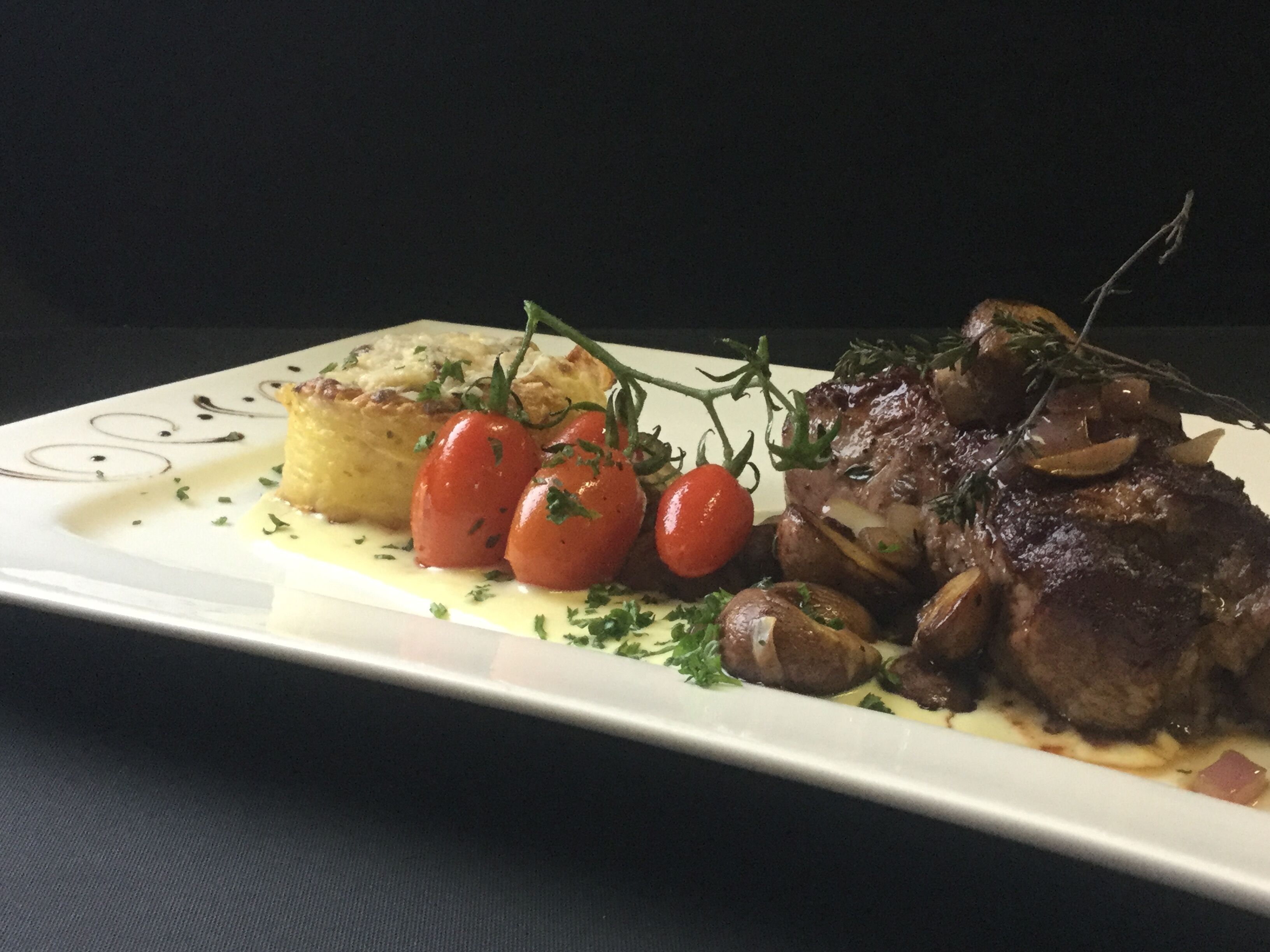 A plate with a steak, cherry tomatoes, and a side of potatoes.