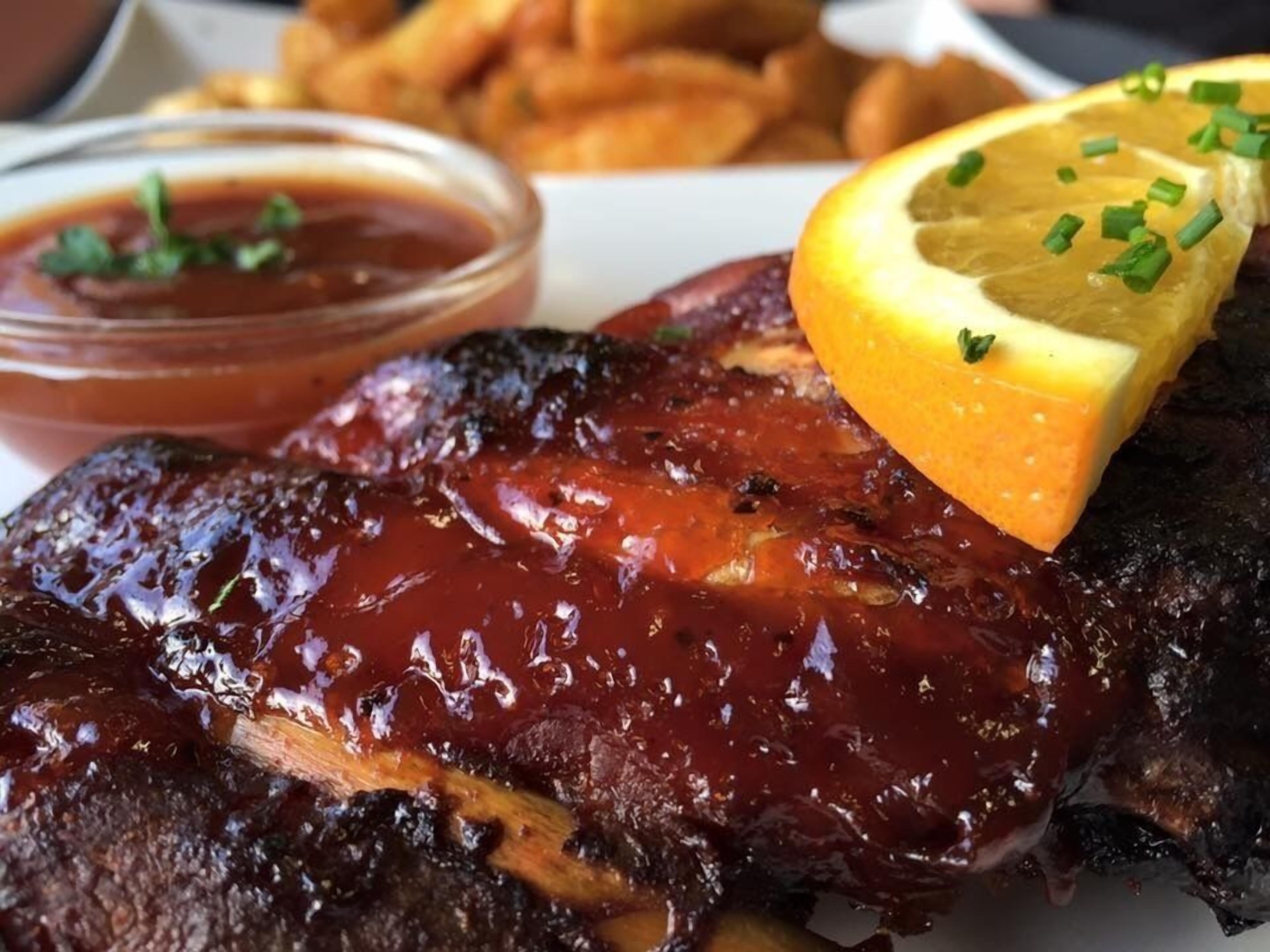 Une assiette de travers de porc grillés, une tranche de citron et une portion de frites.