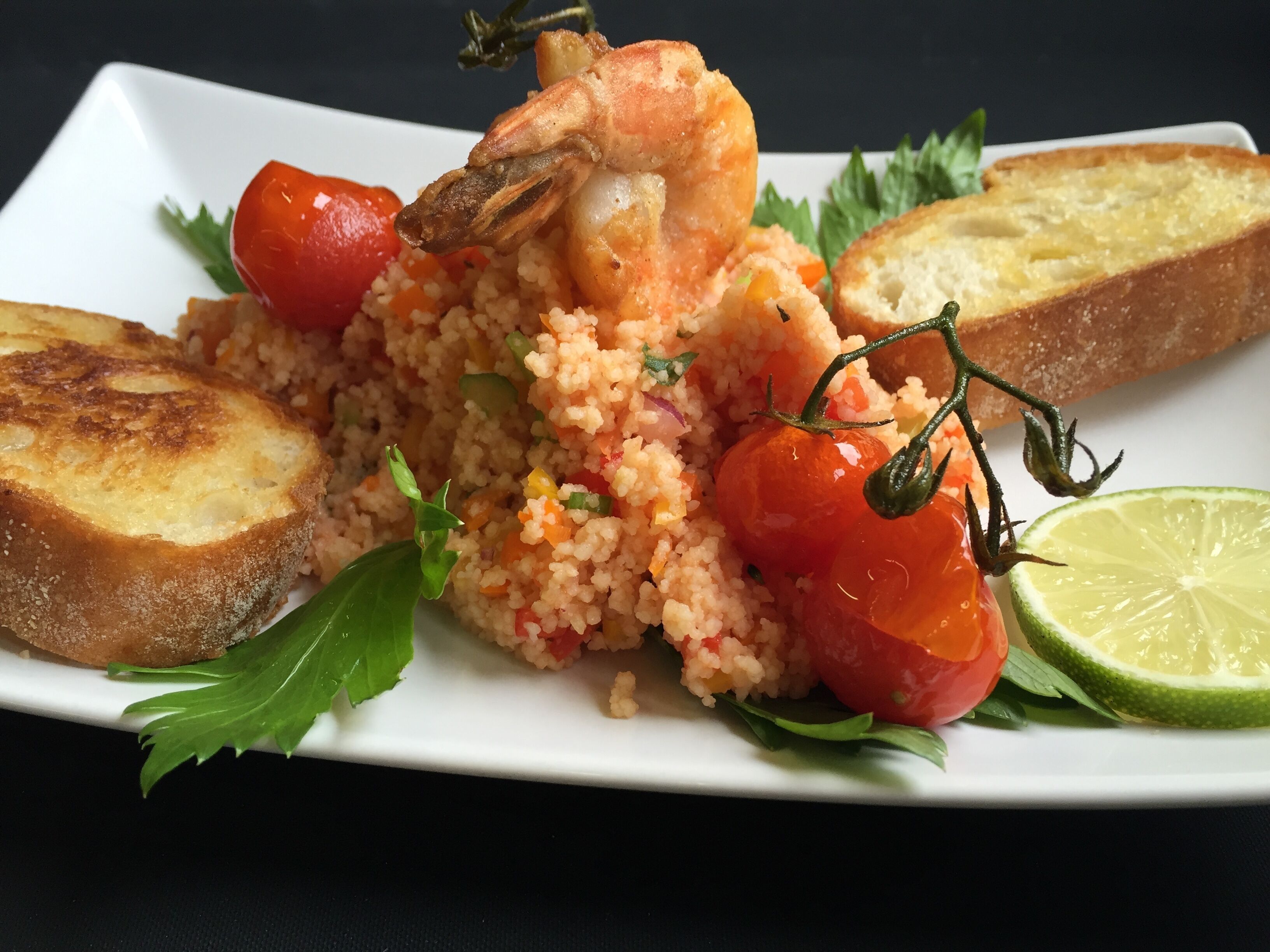 Um prato de comida com arroz, camarão, tomate cereja e pão.