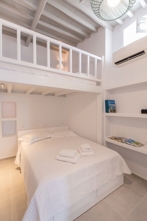 A bedroom with a bunk bed, a bedside table with books, and a wall-mounted air conditioner.